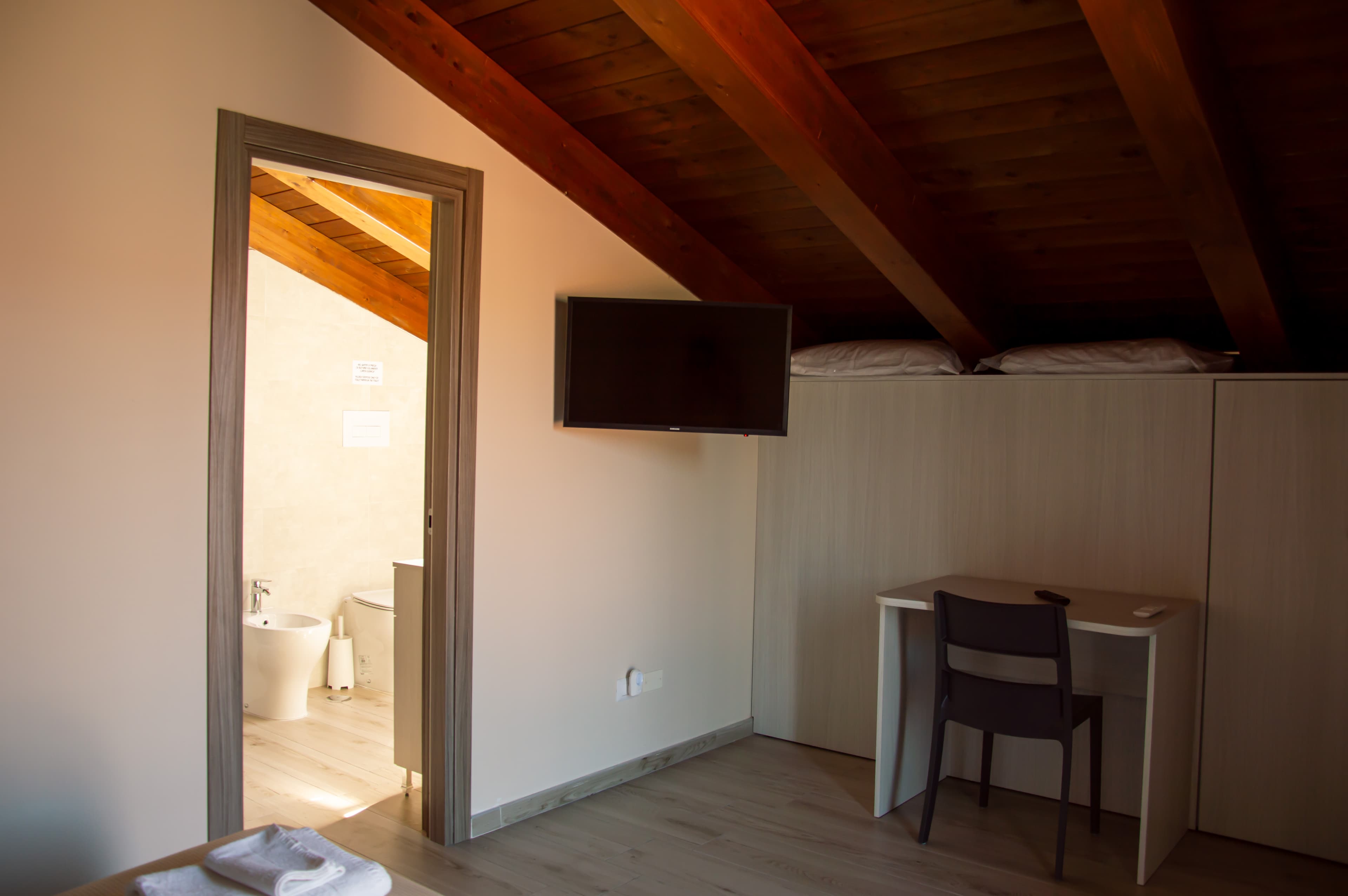 Vista d'insieme della camera matrimoniale, con il soffitto a travi in legno e l'accesso al bagno privato.